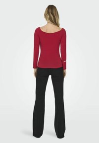 Crvena košulja s dugim rukavima i otvorenim izrezom, uskog kroja s detaljima na manžetama, u kombinaciji s crnim širokim trapericama, prikazana sa stražnje strane.