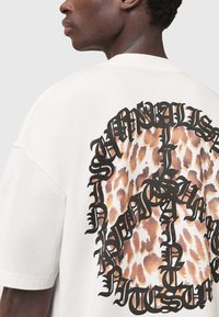 Overdimensioneret cremet T-shirt med en leopardprint grafik omgivet af fed sort tekst. Korte ærmer og rund halsudskæring. Blød stofstruktur.