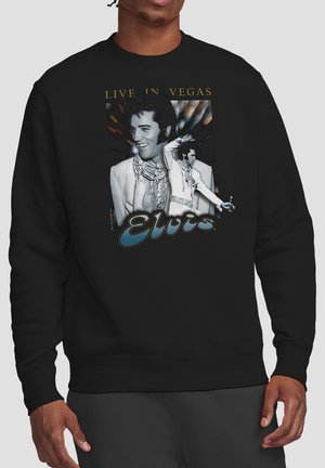 Schwarzer Sweatshirt mit Vintage-Print von Elvis Presley „Live in Vegas“, der zwei Schwarz-Weiß-Bilder von Elvis in einem weißen, verzierten Overall zeigt.