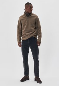 Khaki fleece pullover med en kvart lynlås, struktureret overflade, kombineret med mørke jeans og brune sko, med et enkelt design og klassisk pasform.