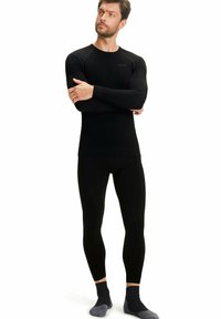 Zwarte langwerpige compressietop met bijpassende leggings, met een gladde textuur en subtiele logo op de borst, gecombineerd met grijze sokken.