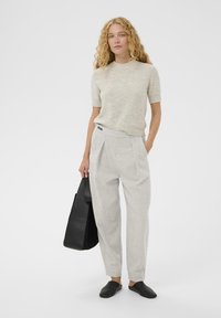 Szürke kötött pulóver rövid ujjakkal, világosszürke, rakott nadrággal párosítva. A megjelenést fekete bőr táska és fekete slip-on cipők teszik teljessé.