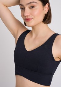 Marineblauwe sport-bh met een V-halsontwerp, brede banden, naaddetails en een elastische tailleband. Gemaakt van een gladde, rekbare stof.