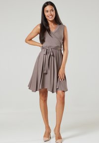 Wrap dress in taupe, sleeveless design with V-neck, cinched waist, flowing skirt, and fabric texture; paired with nude heels.