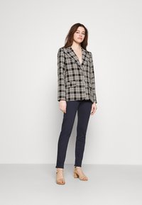 Zwart-wit geruite blazer met een reverskraag, enkele knoopsluiting en twee vo pockets, gecombineerd met marineblauwe slanke broek en tan hakken.