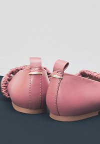 Roze leren ballerina's met een gekruiste rand om de kraag, voorzien van kleine gouden accenten en een lichtbruine zool.
