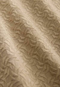 Tissu beige présentant un motif texturé de triangles entrelacés, avec un léger éclat et des détails de broderie subtile tout au long.