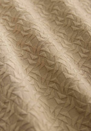 Beige fabric featuring a textured pattern of interwoven triangles, with a slight sheen and subtle embroidery detailing throughout.