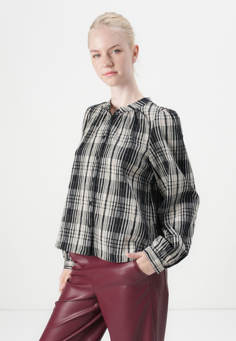 Schwarz-weiße karierte Hemdbluse mit Rundkragen, langen Puffärmeln und einer lockeren Passform. Kombiniert mit burgunderfarbenen kunstledernen Hosen.