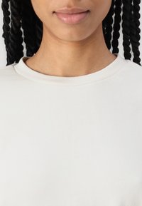 Krämfärgad t-shirt i bomull med rund halsringning och korta ärmar. Slät textur, minimalistisk design utan synliga mönster eller accenter.