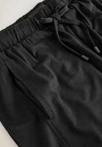 Black cotton shorts with an elastic waistband, drawstring closure, and side pockets. Smooth texture, casual design, suitable for various activities.