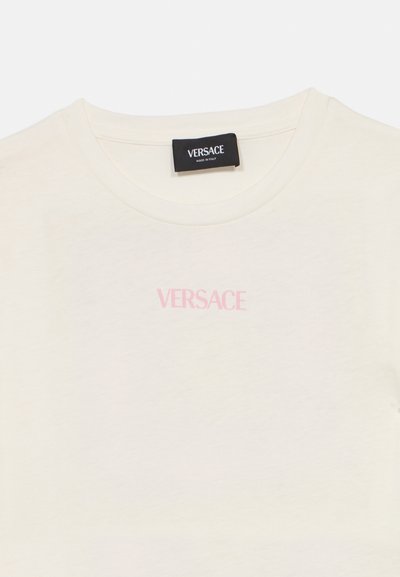 Κρεμ βαμβακερό μπλουζάκι με στρογγυλή λαιμόκοψη, με ένα ανοιχτό ροζ λογότυπο "VERSACE" τυπωμένο μπροστά. Απλή και λεία υφή.