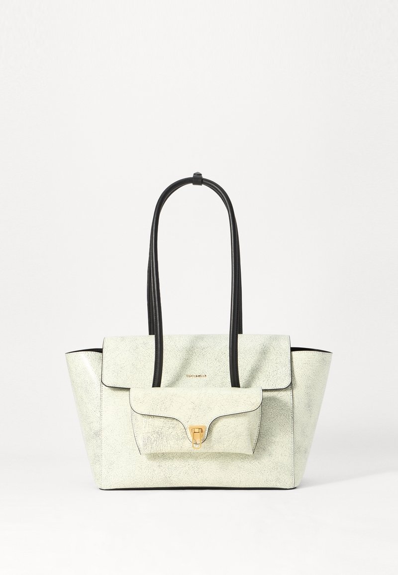 Sac cabas en cuir blanc texturé avec poignées noires, poche avant à rabat avec fermoir doré et logo du créateur sur le rabat supérieur.