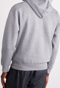 Felpa grigia con tasca a marsupio, cappuccio con lacci e polsini e bordo a costine. Texture morbida e vestibilità rilassata mostrata da dietro.