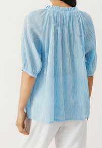 Hellbluse mit Streifen, Gathered-Ausschnitt und kurzen Puffärmeln; aus einem leichten, strukturierten Stoff gefertigt. Lässige Passform.