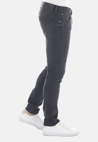 Vaqueros slim fit para hombre en denim gris oscuro, con cinco bolsillos, presillas para el cinturón y una cinturilla negra texturizada, combinados con zapatillas blancas.