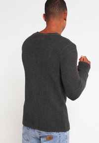 Dunkelgrauer Pullover mit strukturiertem Strick, rundem Ausschnitt und langen Ärmeln. Die Rückansicht zeigt ein tailliertes Design mit gerippten Details und einer dezenten Naht.