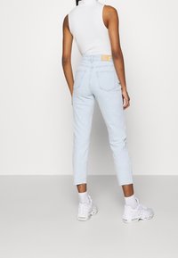 Jeans de tiro alto en azul claro con un dobladillo recortado, cinco bolsillos y una etiqueta en la parte de atrás, combinados con zapatillas blancas y calcetines tobilleros.