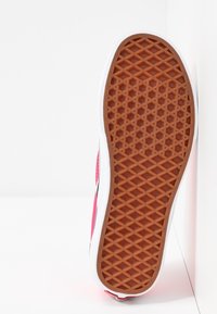 Semelle d'une basket rose montrant une accroche brun motif gaufré et une semelle intermédiaire blanche sur fond blanc uni.