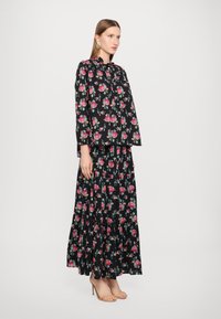 Blomstermønstrete bluse og maxiskjørt sett i svart med rosa og grønne roser. Løs passform, lange ermer, lagdelt skjørt, myk stoff, hæler.
