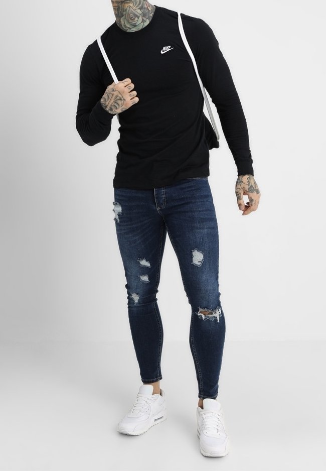 Musta pitkähihaine Nike-paita, kuluneet siniset farkut repeämillä ja valkoiset tennarit. Lisäksi näkyvissä tatuoidut kädet ja hihnat paidassa.