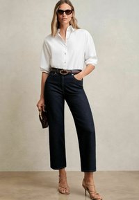 Vit skjorta med knappar, mörka denimbyxor med vida ben, brunt bälte med guldfäste, brun handväska, beige strappy klackar och solglasögon.