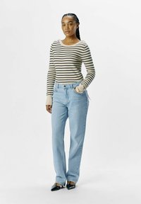 Stribet sweater i beige og sort, høj talje blå jeans, tætsiddende ved taljen, vide ved benene, og sorte spidse hæle.