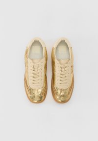 Gold leather sneakers with a textured finish, beige accents, and classic lace-up design. Rubber sole with light brown traction.