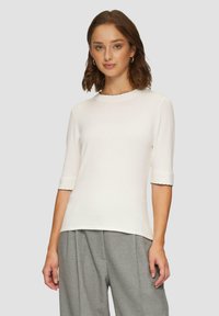 Witte top met korte mouwen en een scalloped rand aan de halslijn en mouwen. Gemaakt van een zachte, gestructureerde stof. Gecombineerd met een grijze geplooide broek.