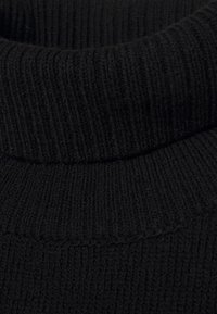 Pull noir à col roulé côtelé avec un col montant et un tissu texturé. Vue en gros plan mettant en valeur le tissage et la douceur du matériau.