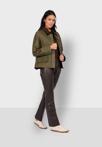 Oliwkowa skórzana kurtka z brązowym kołnierzem, dwoma przednimi kieszeniami i zatrzaskami. Połączona z ciemnobrązowymi skórzanymi spodniami i beżowymi trampkami.