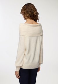 Maglione oversize color crema con colletto a coste a spalle scoperte, lunghe maniche a sbuffo e fascia a coste in vita. Tessuto morbido e con texture.