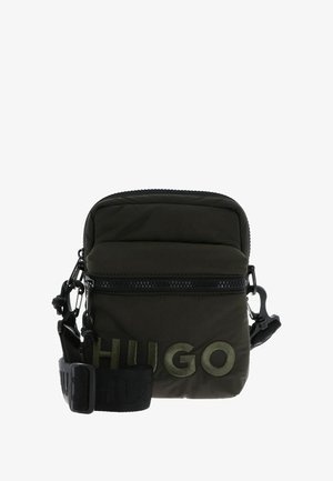 Bolso bandolera compacto de color verde oscuro con correa negra ajustable y gran logo bordado "HUGO" en el bolsillo frontal.