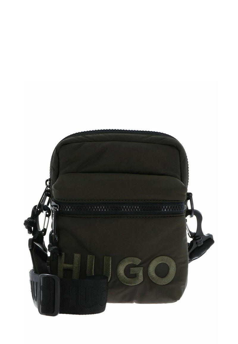 Piccola borsa a tracolla verde scuro con tracolla nera regolabile e grande logo "HUGO" ricamato sulla tasca frontale.