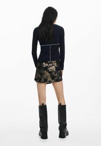 Mornarska bluza dugih rukava s bijelim šavovima, u kombinaciji s mini suknjom s crno-zlatnim uzorkom i crnim čizmama do koljena.