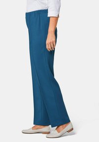 Teal, elastische taillebroek met een rechte pijp. Beschikt over een gladde textuur en diepe kleur, gecombineerd met lichtgekleurde platte schoenen.