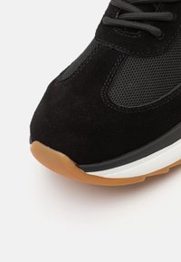 Bout de basket noir avec dessus en suédé et mesh, lacets noirs, semelle intermédiaire blanche et semelle extérieure en caoutchouc naturel sur fond blanc.