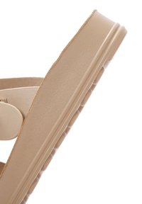 Beige slip-on sandal with a textured rubber sole, rounded toe, and a wide strap featuring a circular accent.