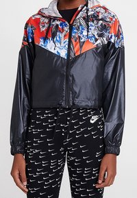 Lehká bomber bunda černé barvy s květinovým designem v červené a modré na kapuci, s uzávěrem na zip a stahovací spodní částí. V kombinaci s vzorovanými legínami.