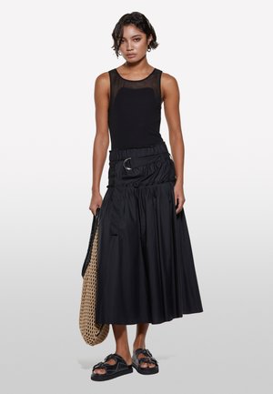 Haut sans manches noir avec un panneau transparent et une longue jupe noire dotée d'une taille élastique et d'un détail de ceinture, associée à des sandales noires.