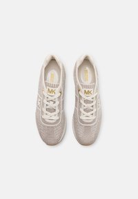 Scarpe atletiche beige chiaro con una parte superiore in maglia testurizzata, lacci bianchi e dettagli dorati. Presentano una suola imbottita e accenti con il logo.