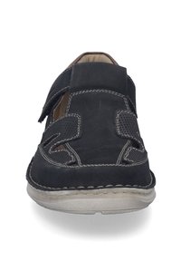 Sort lædersko med velcro-strimler, åbne sider og synlige sømme. Har en flad gummisål med en tekstureret overflade.