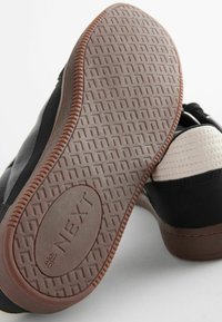 Scarpe da ginnastica nere e crema con tomaia in pelle testurizzata, suola in gomma marrone con motivo a diamante e logo marchiato al centro.