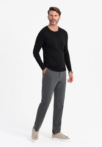 Schwarzes, langes Strickshirt, graue, maßgeschneiderte Hose und beiger Sneakers. Der Look zeichnet sich durch klare Linien und eine figurnah geschnittene Silhouette aus.