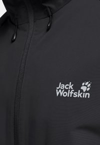 Schwarze wasserdichte Jacke mit Reißverschluss, versehen mit dem "Jack Wolfskin"-Logo und einem Pfotenabdruck in Hellgrau. Mit verstellbarer Kapuze.