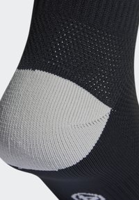 Calcetín negro con una parte superior texturizada, talón reforzado gris y áreas de malla para ventilación y comodidad.