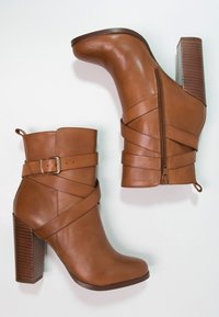 Hnědé kotníkové boty na podpatku z hladké kůže, s překříženými pásky, bočním zipem a texturovaným vrstveným podpatkem.