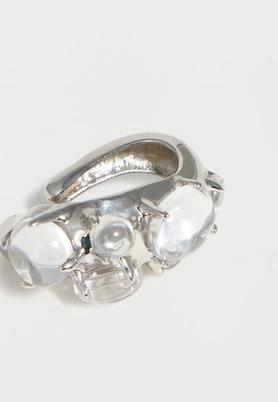 Ασημένιο ρυθμιζόμενο δαχτυλίδι με τρεις καθαρές, στρογγυλεμένες πέτρες σε δαχτυλιδόπλοκα σε απλό λευκό φόντο.