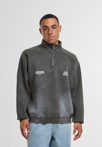 Pullover in pile grigio con colletto a mezza zip, caratterizzato da una trama leggermente sbiadita. Decorato con due piccoli loghi bianchi nella zona del petto.