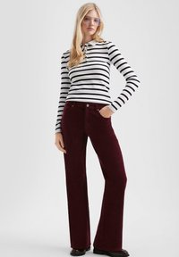 Gestreept zwart-wit longsleeve shirt gecombineerd met bordeaux corduroy flared pants. De broek heeft voorzakken en een knoopsluiting.